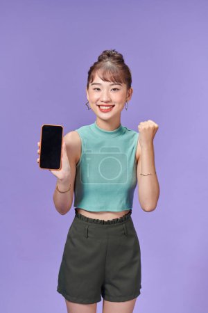 Photo for Young excited woman hold mobile phone with blank screen and winner gesture - Royalty Free Image