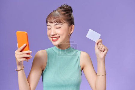 Foto de Chica sonriente sosteniendo una tarjeta de crédito y teléfono móvil compras en línea - Imagen libre de derechos
