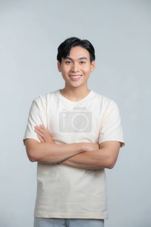 Foto de Sonriente joven asiático con los brazos cruzados sobre un fondo blanco - Imagen libre de derechos