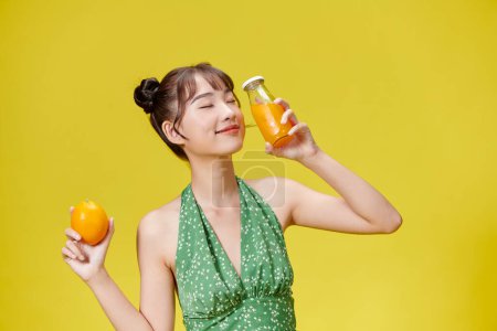 Téléchargez les photos : Gros plan, femme souriante avec du jus d'orange sur fond jaune - en image libre de droit