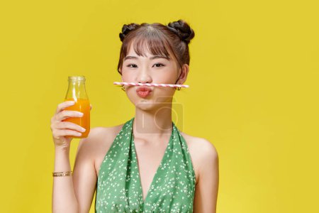 Téléchargez les photos : Jeune femme asiatique tenant jus d'orange frais de bouteille, passer du temps avec plaisir à l'intérieur - en image libre de droit
