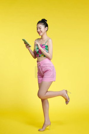 Photo for Relaxed pretty woman in crop top  surfing on smartphone on yellow background - Royalty Free Image