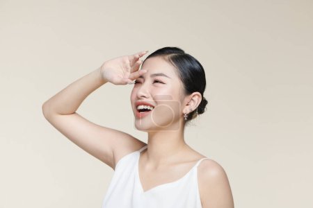 Téléchargez les photos : Young asian woman raising hand to covering her face from sunlight against a beige background - en image libre de droit