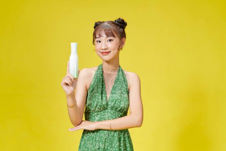 Foto de Retrato de una hermosa mujer sosteniendo la botella con cosméticos mientras está de pie aislado sobre el fondo amarillo - Imagen libre de derechos