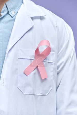 Photo for Casian doctor man with a pink ribbon for the breast cancer awareness pinned in the flap of his white coat - Royalty Free Image