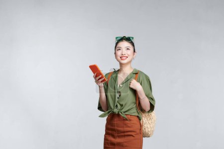 Téléchargez les photos : Femme asiatique voyageur tenant téléphone mobile et concept de voyage d'été sur fond gris - en image libre de droit