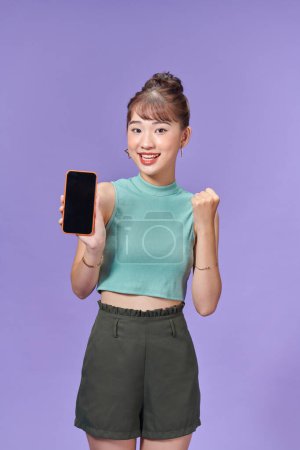 Photo for Young Asian woman holding phone with cheerful face on purple background - Royalty Free Image