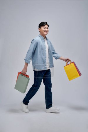 Foto de Retrato de un hombre sonriente sosteniendo bolsas de compras sobre fondo gris y mirando a la cámara - Imagen libre de derechos
