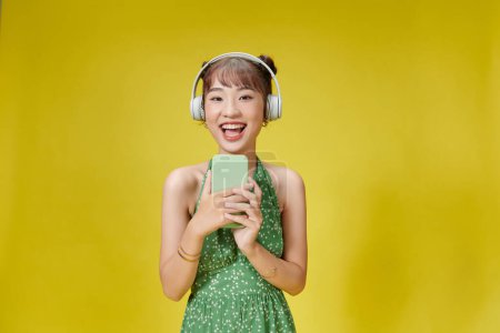Foto de Mujer joven escuchando música sosteniendo teléfono aislado color amarillo fondo - Imagen libre de derechos