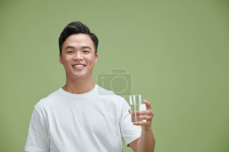 Foto de Handsome young man in a white T-shirt holding a glass of drinking water - Imagen libre de derechos