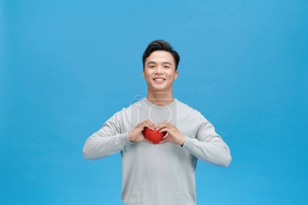 Photo for Young man holding red heart over blue background - Royalty Free Image