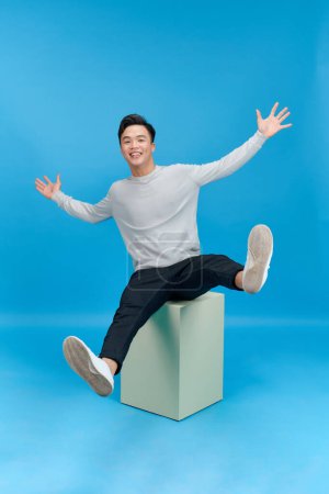 Photo for Full length photo of nice young guy sit white cube copyspace falling back over blue - Royalty Free Image