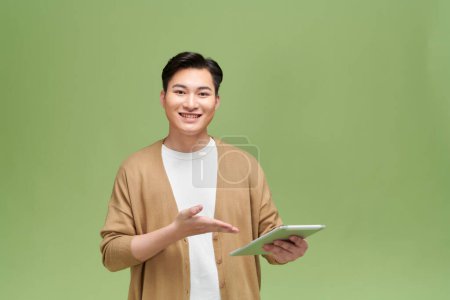 Téléchargez les photos : Portrait d'un homme asiatique excité montrant et présentant avec une tablette dans sa main - en image libre de droit