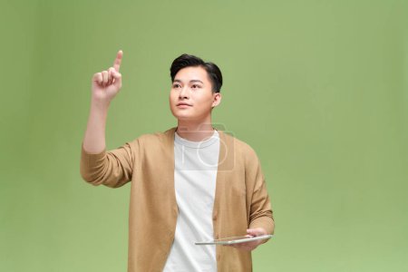 Foto de Retrato de un hombre asiático excitado sostiene la tableta en su mano, levanta la mano, señala al aire - Imagen libre de derechos