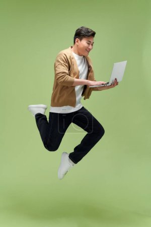Photo for Full length photo of positive man jumping high holding device  isolated green color background - Royalty Free Image