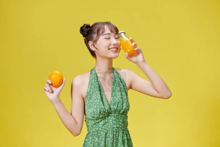 Téléchargez les photos : Portrait d'une jeune femme tenant une orange et un verre de jus d'orange frais - en image libre de droit
