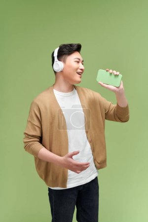 Téléchargez les photos : Jeune homme asiatique chante joyeusement sa chanson préférée. Il tient un smartphone - en image libre de droit