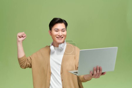Téléchargez les photos : Jeune homme heureux tenant sur l'ordinateur portable et montrant un geste oui - en image libre de droit