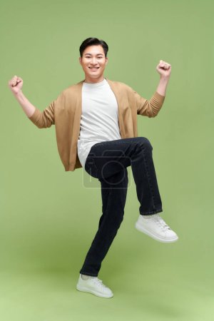 Foto de Longitud completa de un joven satisfecho celebrando el éxito aislado sobre fondo verde - Imagen libre de derechos