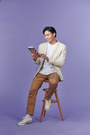 Téléchargez les photos : Happy attractive young man standing and using tablet over purple background - en image libre de droit