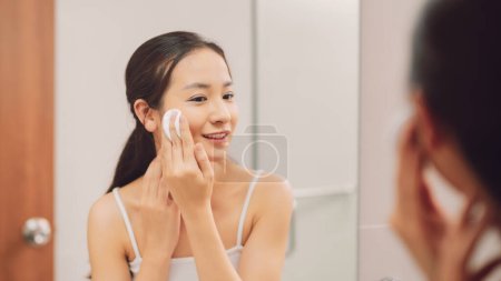 Téléchargez les photos : Femme essuyant son visage avec du coton dans la salle de bain - en image libre de droit