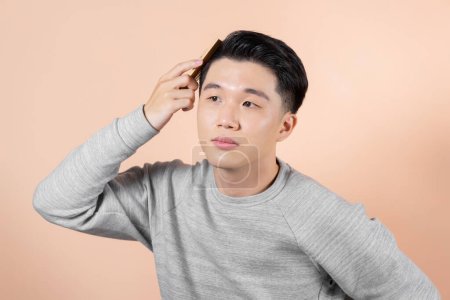 Photo for Handsome young man combing his hair on beige background - Royalty Free Image