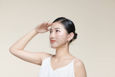 Téléchargez les photos : Jeune femme asiatique couvre son visage du soleil avec la paume sur un fond beige - en image libre de droit