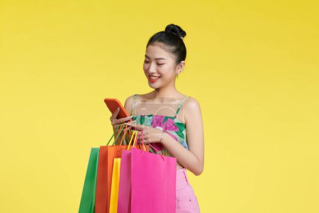 Photo for Portrait of a young woman using mobile phone with shopping bags in her hands. - Royalty Free Image