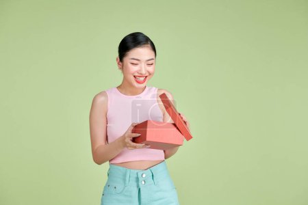 Foto de Retrato de una feliz chica sonriente abriendo una caja de regalo aislada sobre fondo verde - Imagen libre de derechos