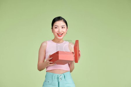 Photo for Happy young woman opening present for Valentine's Day on green studio background, - Royalty Free Image