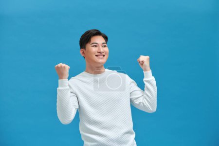 Photo for Cheerful excited man standing isolated over blue background, celebrating success - Royalty Free Image