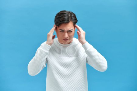 Photo for Asian young man looks upset and squeezing head with hands from a headache - Royalty Free Image