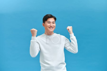 Photo for Happy guy rejoicing and clenching fists like winner or lucky person, isolated over blue background - Royalty Free Image