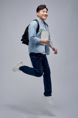 Foto de Longitud completa de un sonriente joven asiático hombre sosteniendo libros, saltando - Imagen libre de derechos