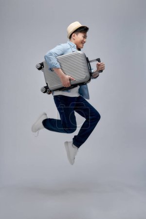 Foto de Largura completa vista lateral de viajero alegre hombre turístico en ropa de verano, saltar corriendo bodega maleta aislada - Imagen libre de derechos