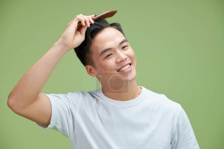 Téléchargez les photos : Concept de personnes - sourire jeune homme brossant les cheveux avec peigne sur fond vert - en image libre de droit