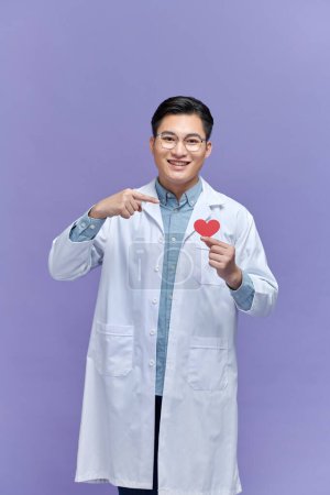 Photo for Handsome young doctor man holding paper with red heart, very happy pointing with hand and finger - Royalty Free Image
