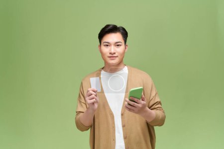 Téléchargez les photos : Jeune homme tient carte de crédit et smartphone isolé sur fond vert - en image libre de droit