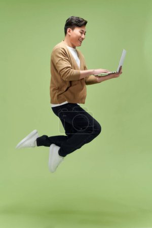 Foto de Foto de perfil de chico deportivo activo salto mantenga netbook trabajo aislado color verde fondo - Imagen libre de derechos