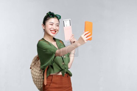 Téléchargez les photos : Une femme souriante prenant un selfie tout en tenant un passeport avec billet d'avion sur fond blanc - en image libre de droit