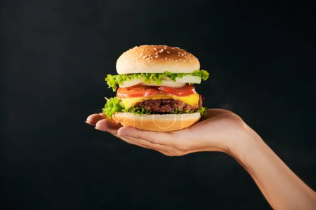Foto de Sabroso sándwich de hamburguesa en mano aislado sobre fondo negro - Imagen libre de derechos