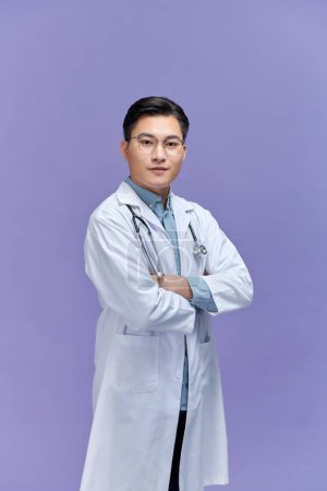Foto de Médico posando con los brazos cruzados, personal médico trabajando sobre fondo púrpura. - Imagen libre de derechos