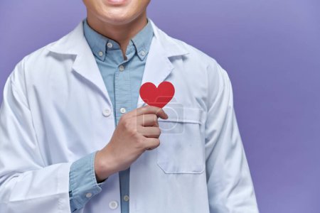 Foto de Médico sosteniendo forma de corazón rojo contra fondo púrpura - Imagen libre de derechos