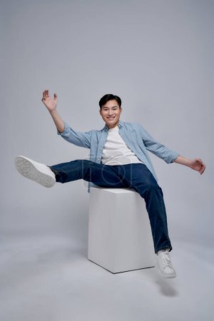 Téléchargez les photos : Jeune homme asiatique assis sur le fond - en image libre de droit