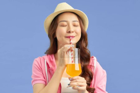 Téléchargez les photos : Jeune belle femme en vacances portant un chapeau d'été boire du jus d'orange - en image libre de droit