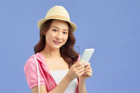 Téléchargez les photos : Asiatique jolie femme touriste préparation pour Voyage et en utilisant smartphone isolé sur fond de bannière bleue. - en image libre de droit