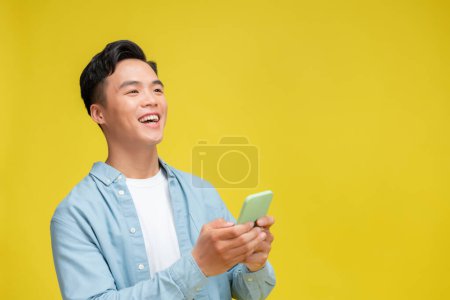 Photo for Shocked young Asian man looking at mobile phone screen reacting to online news with opened mouth - Royalty Free Image