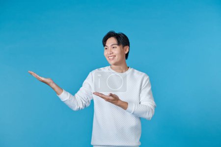 Photo for Attractive Asian man smiling while pointing to his open hand palm - Royalty Free Image