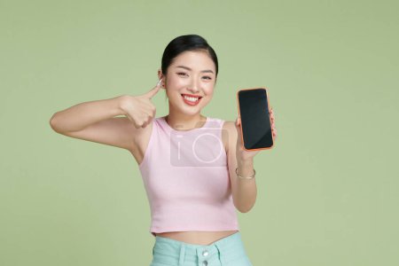 Photo for Satisfied happy asian girl show thumbs-up as demonstrate mobile phone screen application - Royalty Free Image