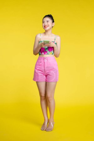 Téléchargez les photos : Belle femme asiatique tenant smartphone et souriant avec mobile, fond jaune clair - en image libre de droit